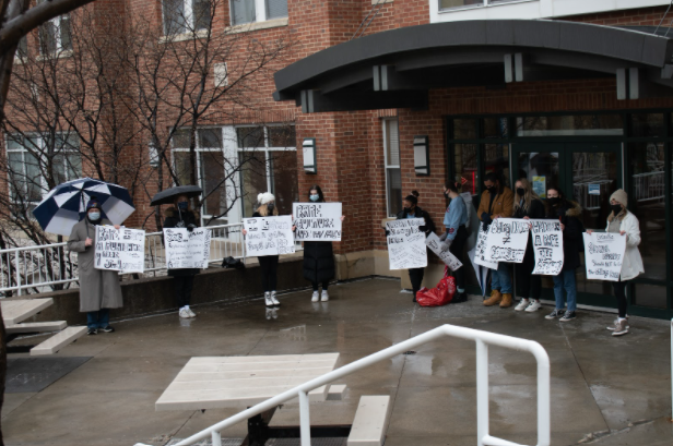 A line of students standing outside of one of UMKCs residence halls with signs in hand.
