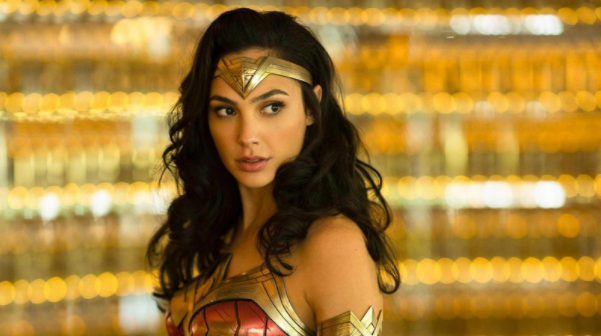 Gal+Gadot%2C+the+actress+that+plays+Wonder+Woman+in+WW84+standing+in+her+wonder+woman+uniform+with+a+gold+background%2C+looking+off+into+the+distance.