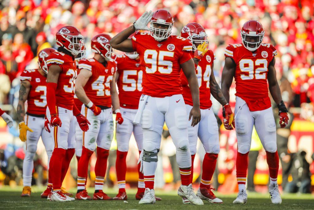 A large group of KC Chiefs players standing around with their helmets on, players 95, 92, 50, 45, and 35 are standing within this group