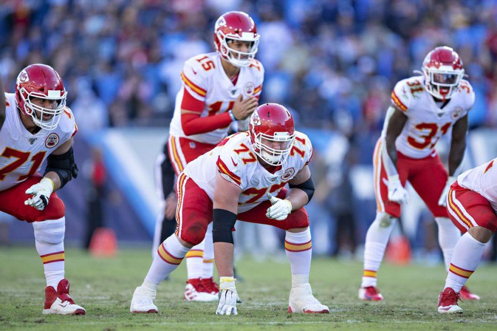 Offensive+line+of+the+Kansas+City+Chiefs+football+team%2C+with+four+leaning+forward+and+Patrick+Mahomes+standing+back+and+up+behind+the+offensive+linemen
