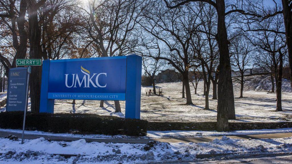 Large Blue sign stating UMKC - University of Missouri Kansas City, surrounded by trees and snows at the front of the UMKC Volker Campus